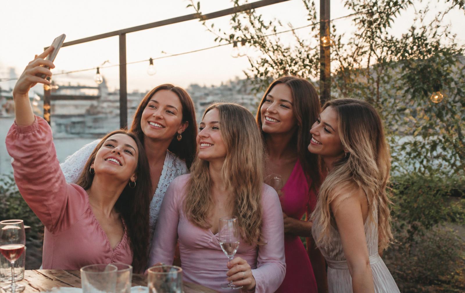 Groep vriendinnen neemt selfie op rooftop terras tijdens vrijgezellenfeest bij zonsondergang