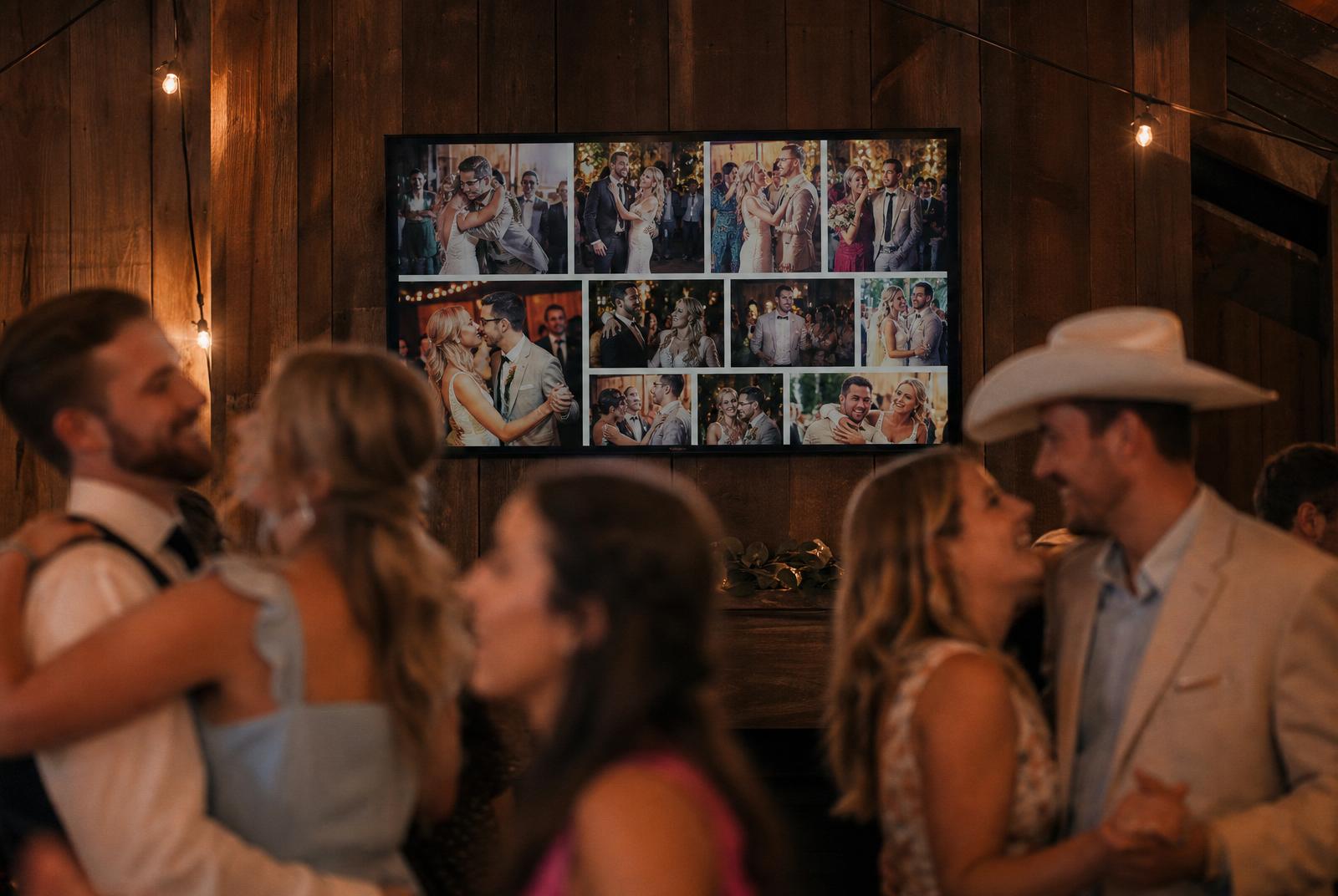 Trouwreceptie met groot scherm dat live slideshow van gastenfoto's toont, gasten dansen op voorgrond